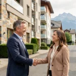Agent immobilier en Isère serrant la main d'un couple devant un immeuble résidentiel avec les montagnes de Chartreuse en arrière-plan